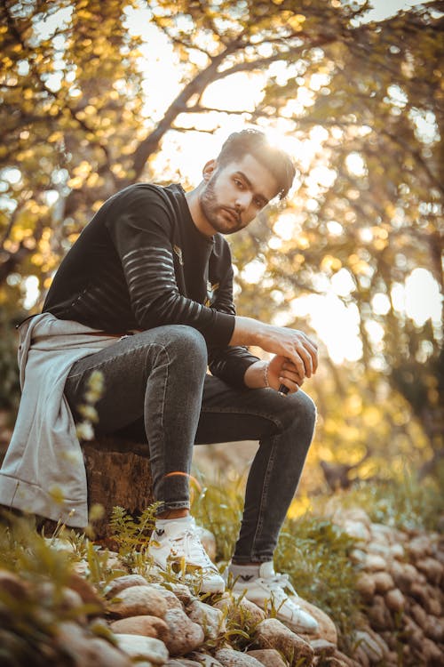 Man In Black Long Sleeve Shirt And Denim Jeans Sitting On Tree Trunk