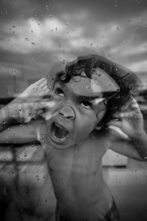 Free Young boy making funny faces behind glass with rain droplets. Stock Photo