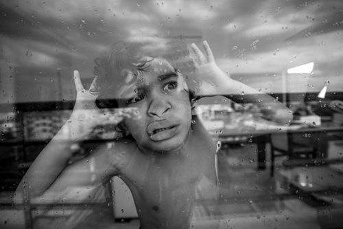 Free Black and white photo of a child looking through a rainy window with curiosity. Stock Photo