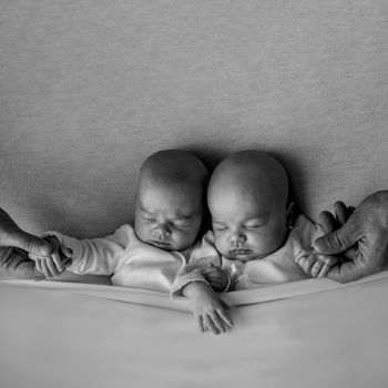 Heartwarming black and white photo of peaceful sleeping twin babies held by adult hands.