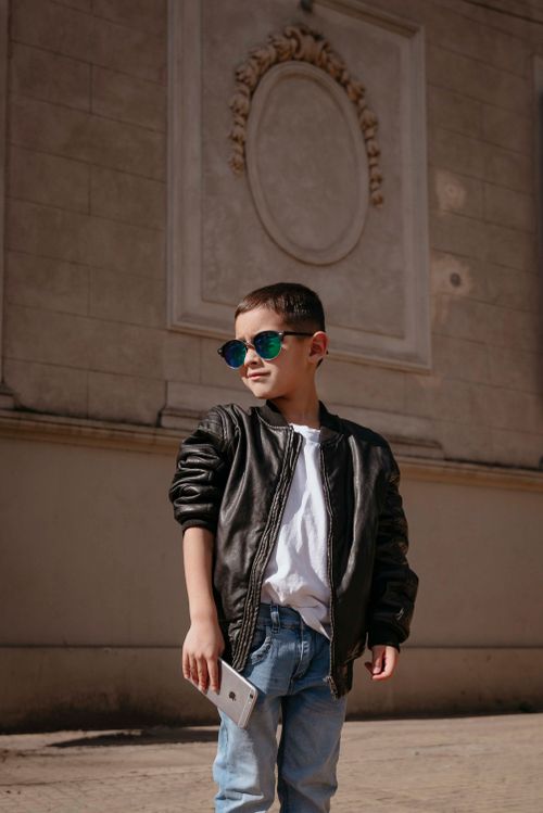 Free Fashionable boy in sunglasses holding phone standing against ornate wall on a sunny day. Stock Photo