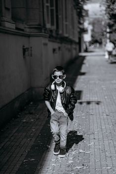 Black and white photo of a cool young boy walking down an urban street in Argentina wearing sunglasses and headphones.