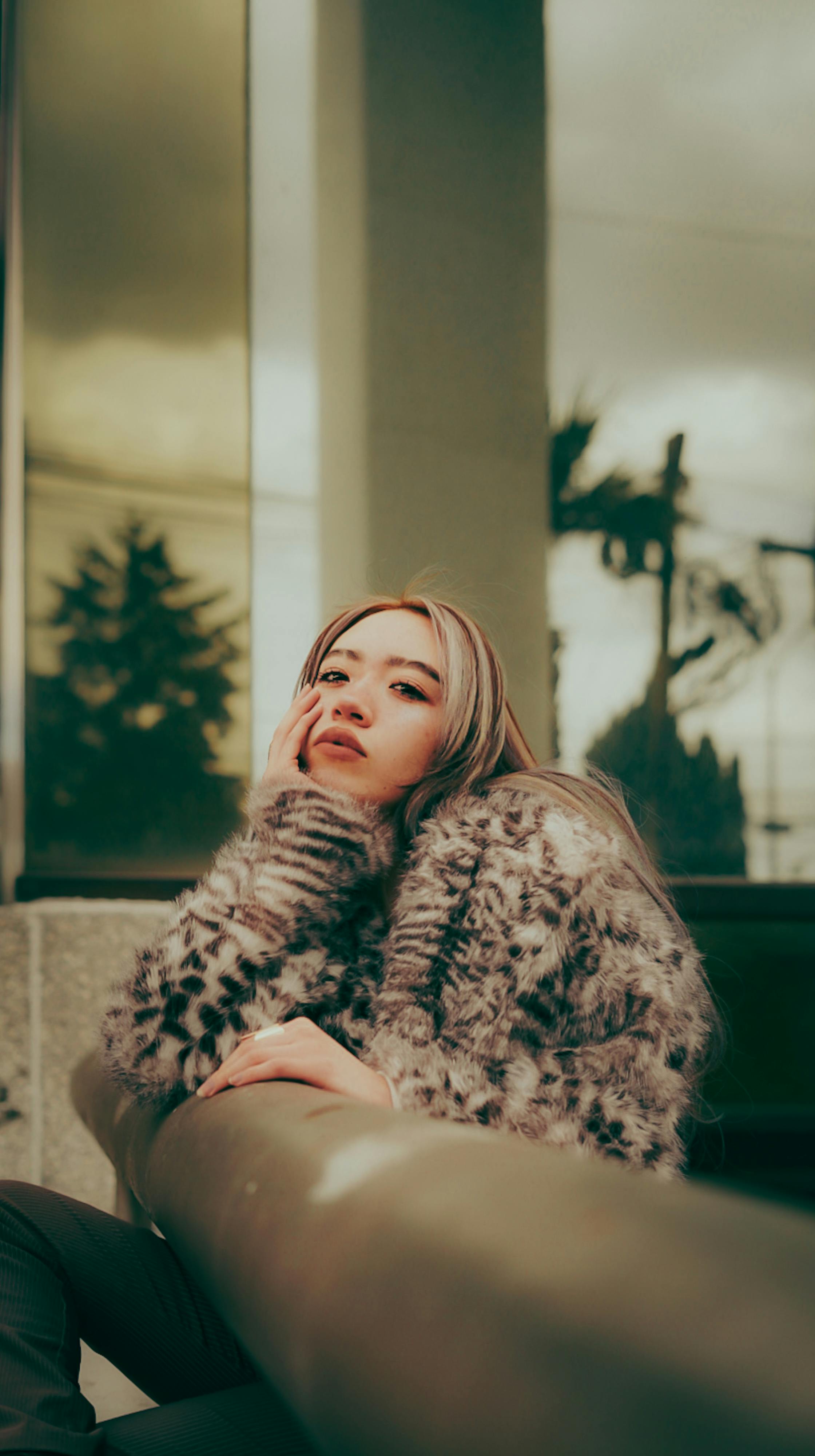 Gratis Una giovane donna alla moda posa con una pelliccia fuori da un edificio moderno, emanando un'atmosfera malinconica. Foto a disposizione