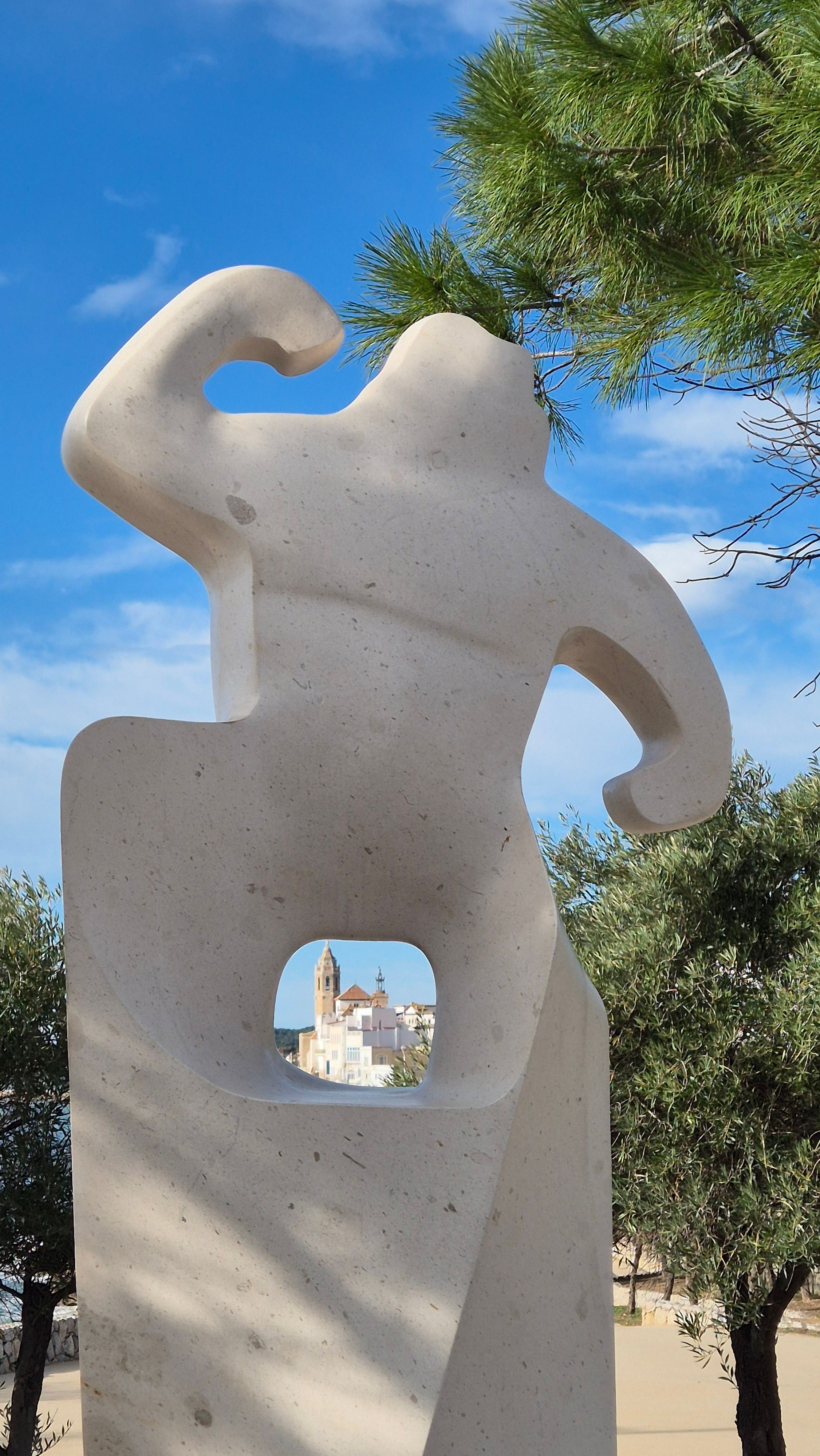 A unique sculpture frames the iconic church in Sitges, Spain, against a blue sky backdrop.