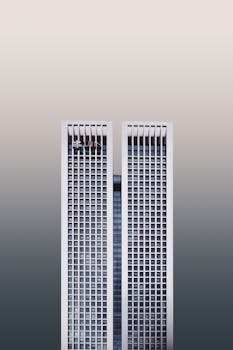 A modern twin skyscraper with a minimalist facade against a neutral sky.