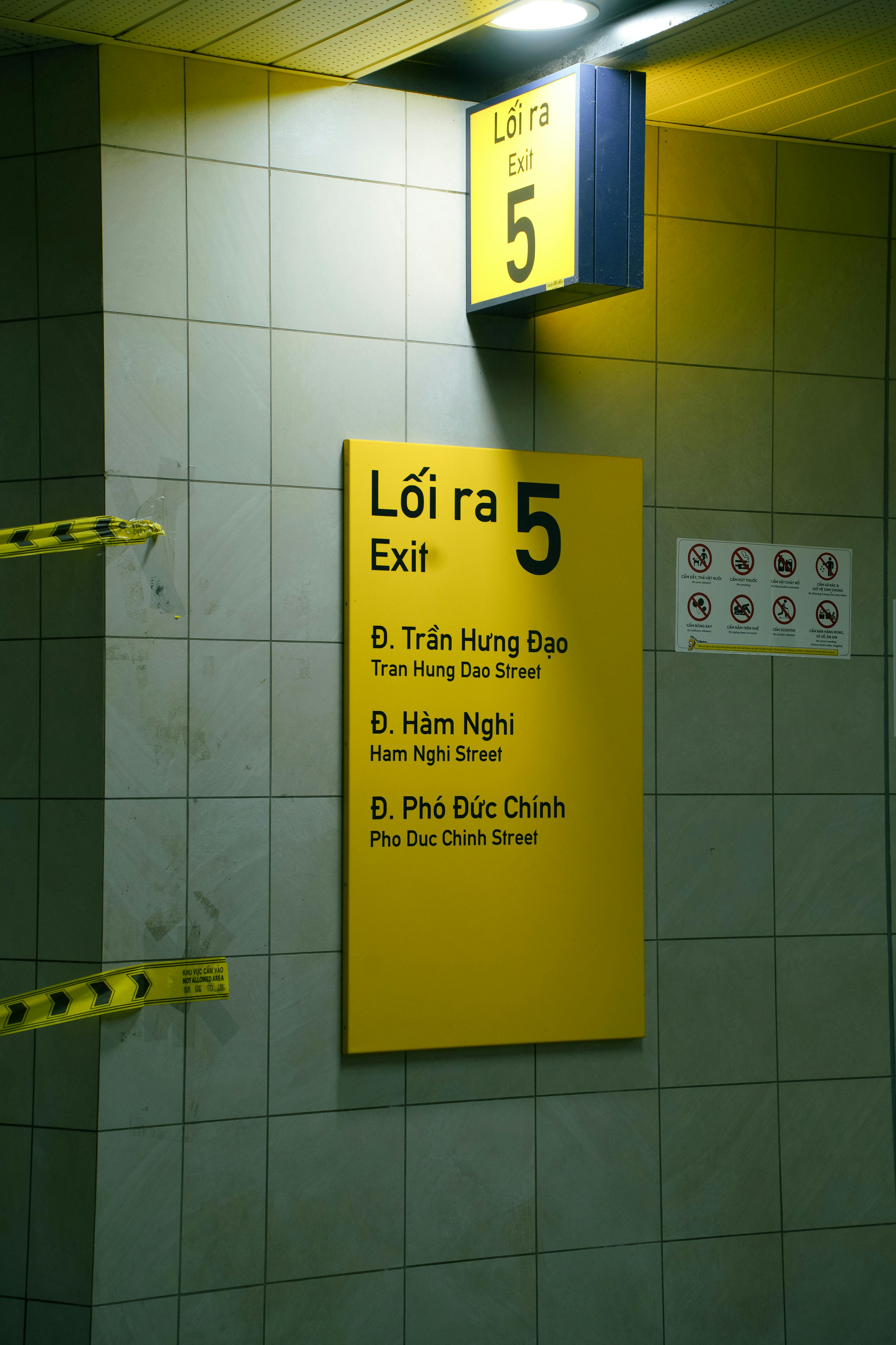 Yellow exit sign in Vietnamese subway station showing directions to nearby streets.