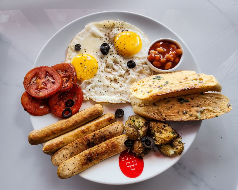 A top-down view of a classic English breakfast featuring fried eggs, sausage, and grilled tomatoes.