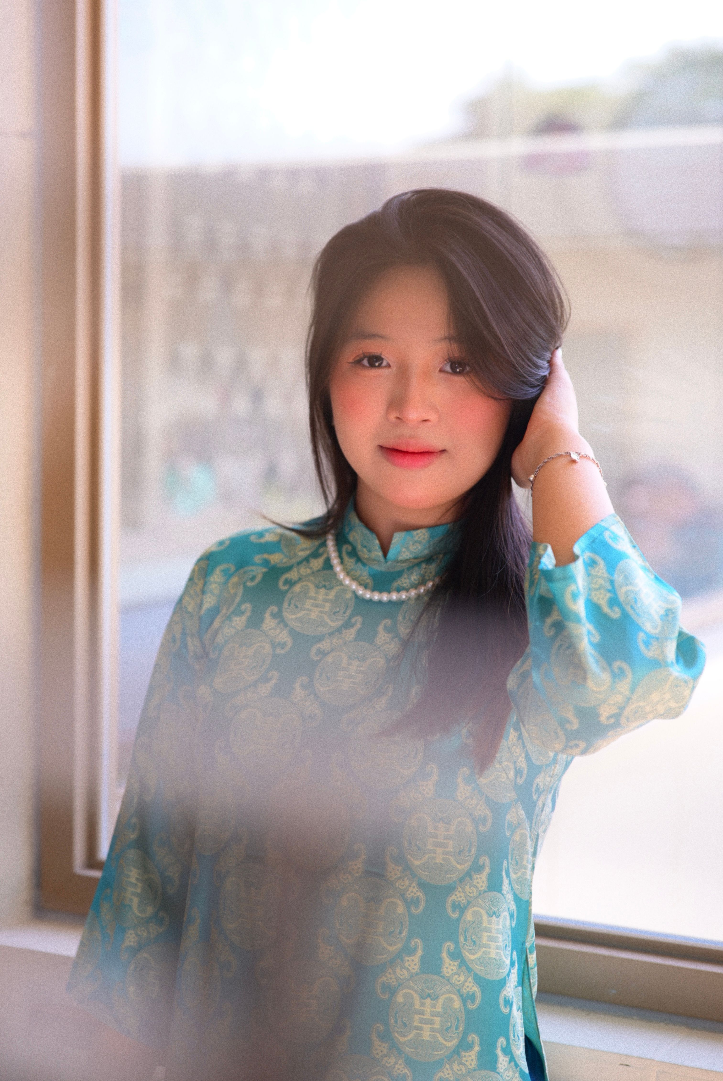 Portrait of a woman in traditional dress smiling gently by a window.