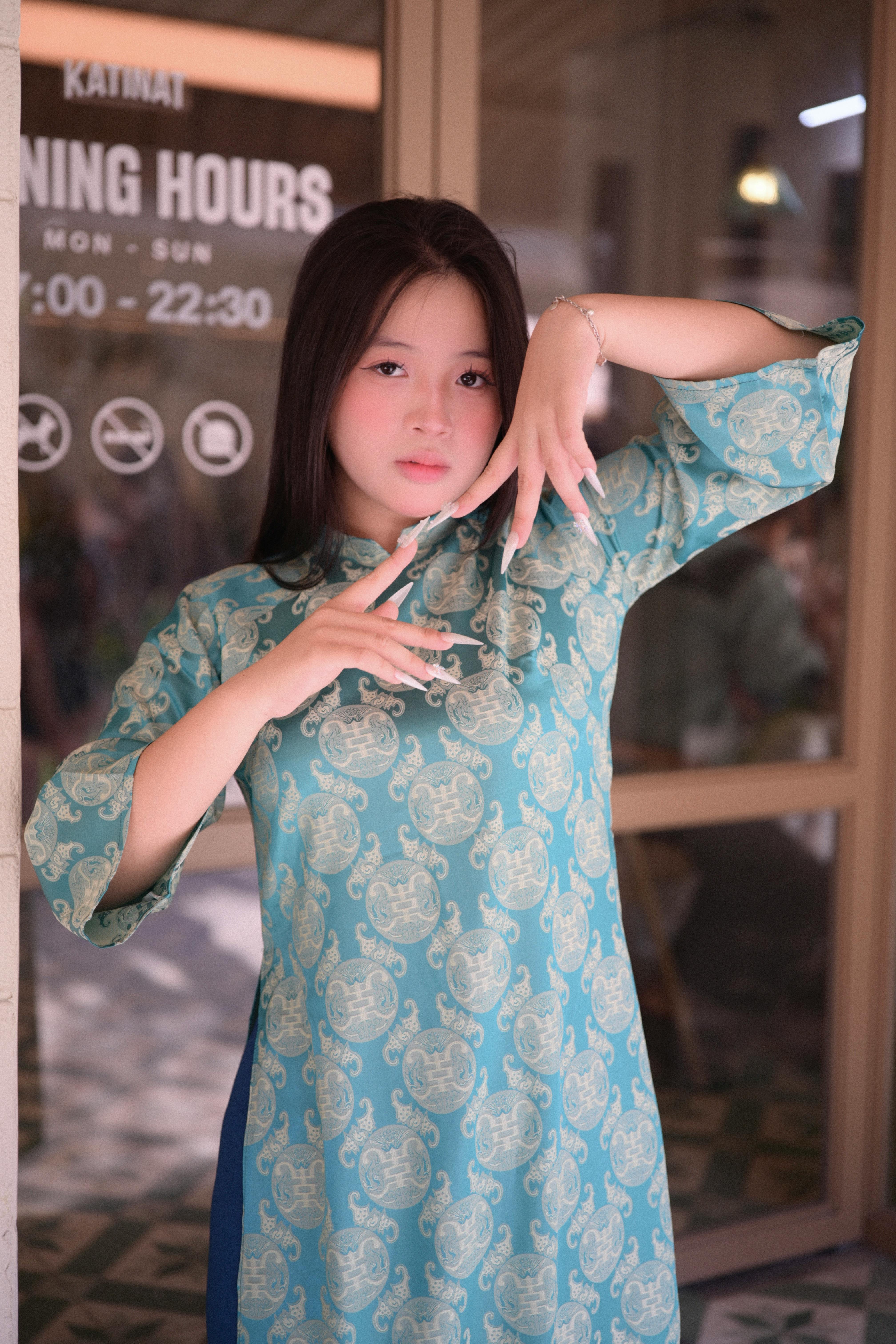 A young woman in a patterned green dress poses gracefully indoors.