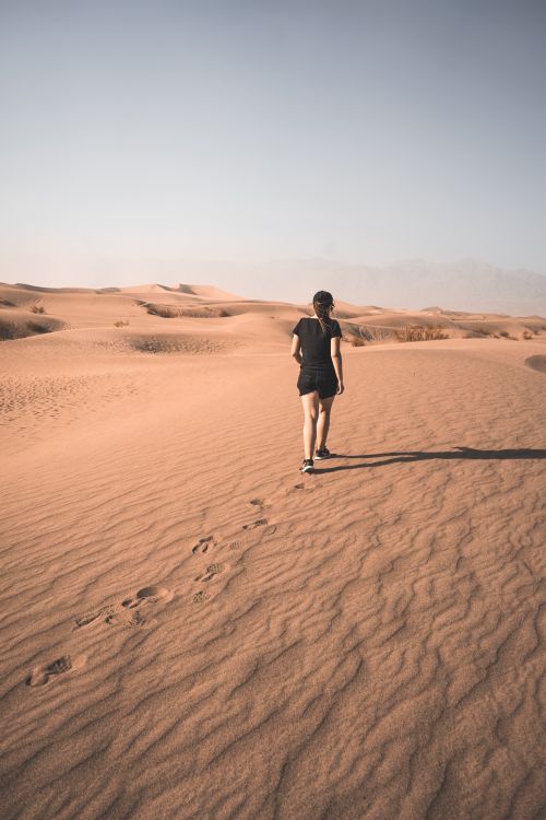 Free Person walking alone in vast desert under clear sky, creating a serene and introspective mood. Stock Photo