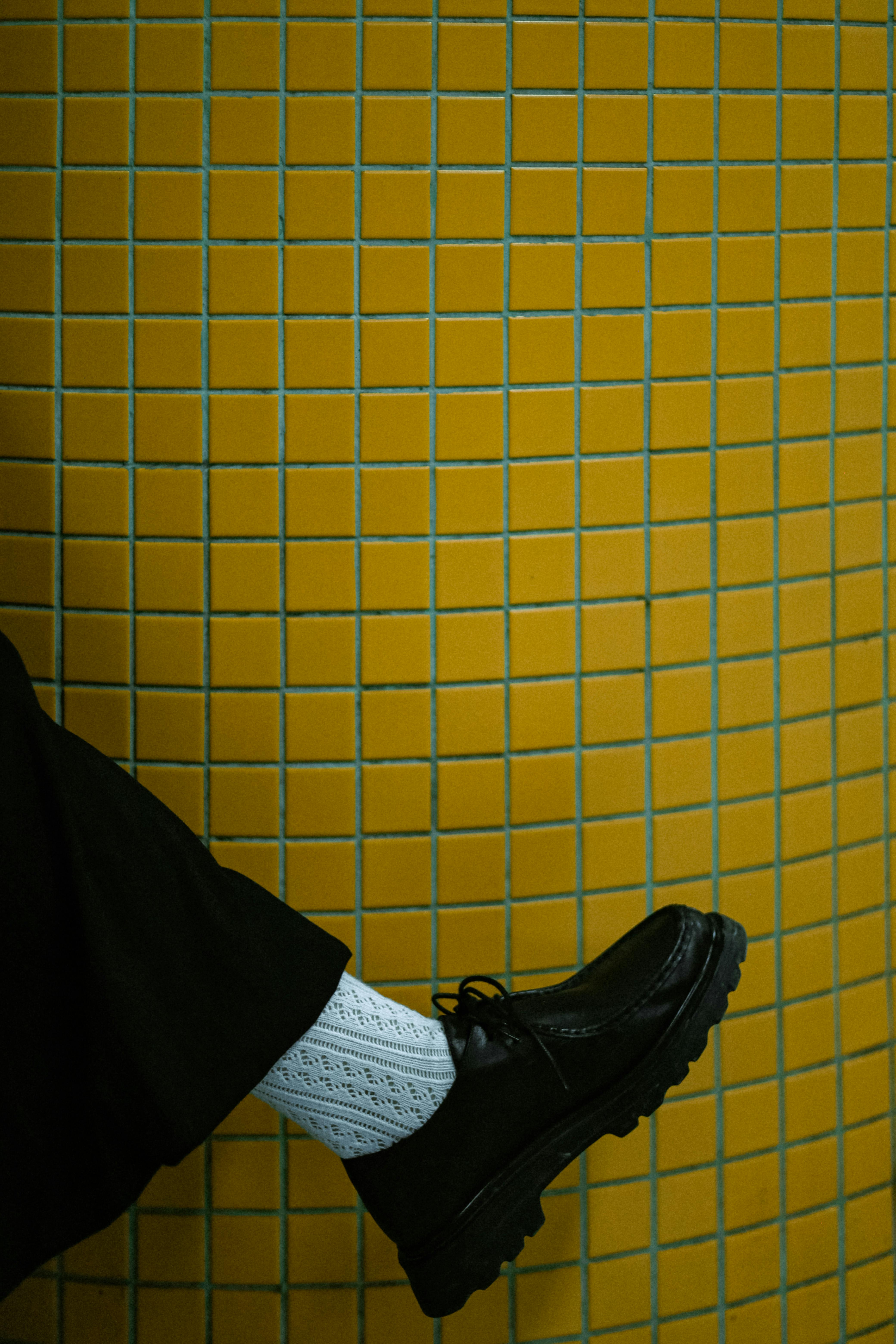無料 鮮やかな黄色のタイルの背景に、黒い靴と白いソックスが映え、スタイルとモダンなファッションを表現しています。 写真素材