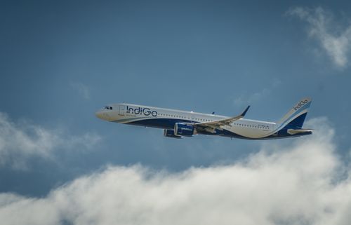 Free IndiGo airline jet cruising through clear blue sky above fluffy clouds. Stock Photo