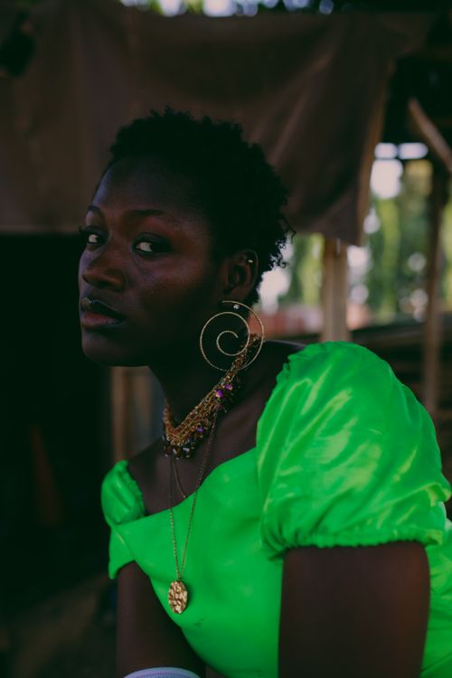 Free A striking portrait of a woman in a vibrant green dress with bold jewelry against an outdoor setting. Stock Photo