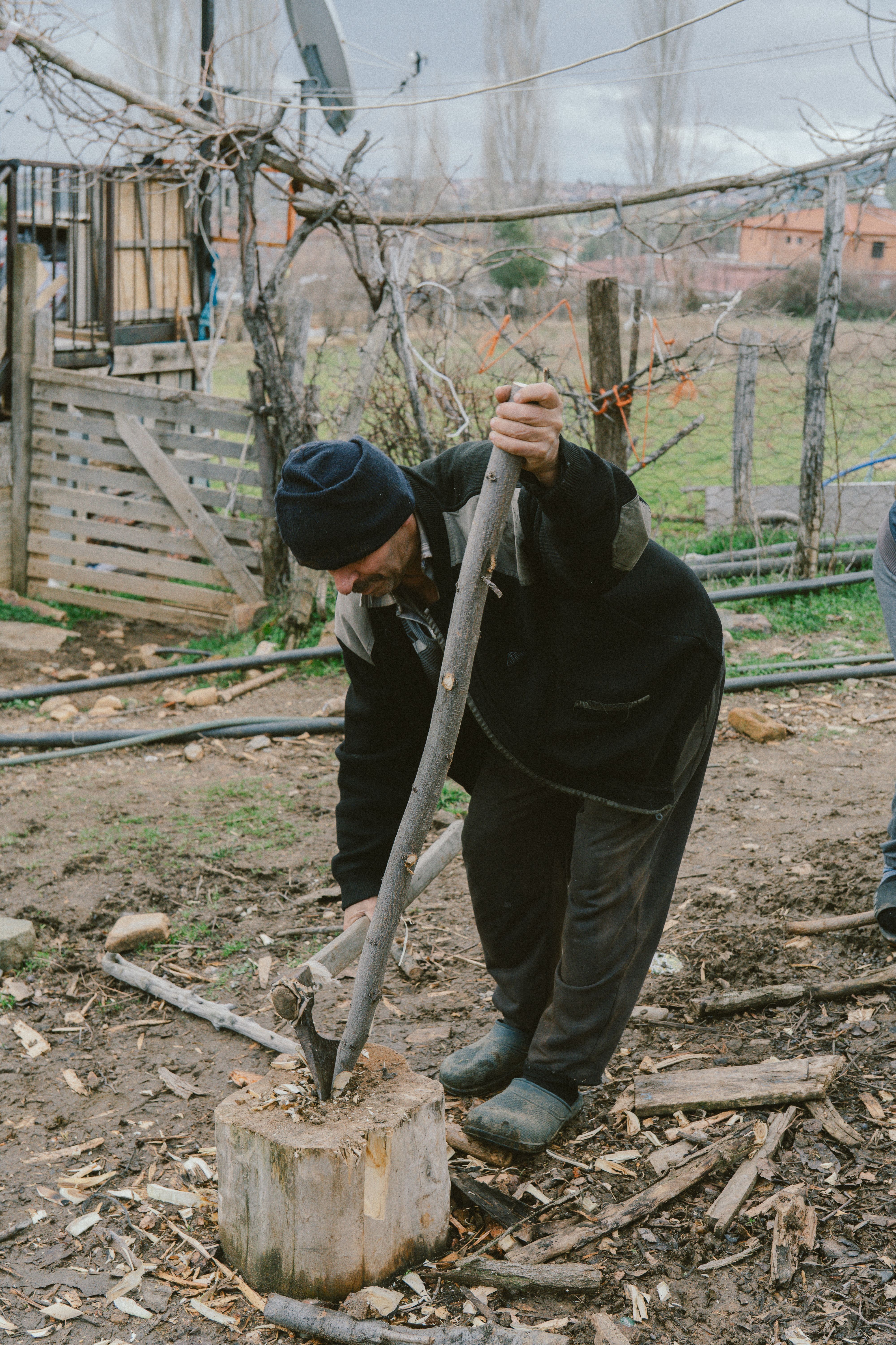 A man outdoors splitting firewood in a rustic rural setting during winter.