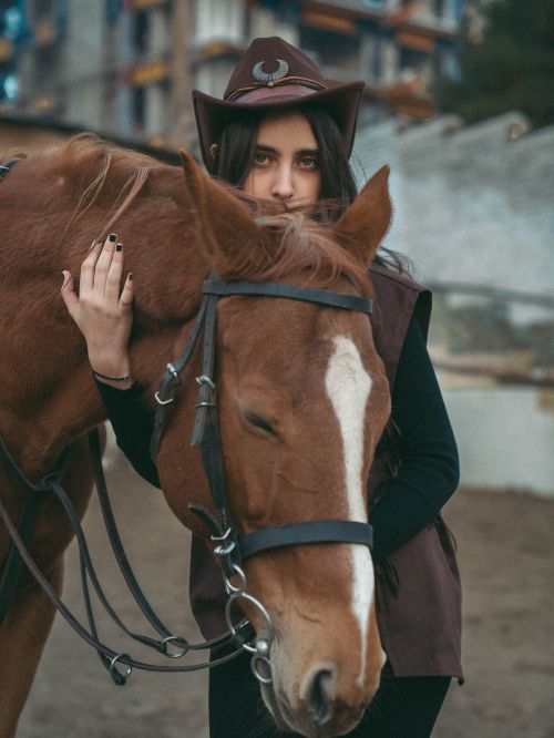 Free A young woman in a cowboy hat embraces a chestnut horse in an outdoor setting, showcasing a bond between human and animal. Stock Photo