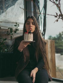 Young woman blowing out candles on cake during outdoor birthday celebration.