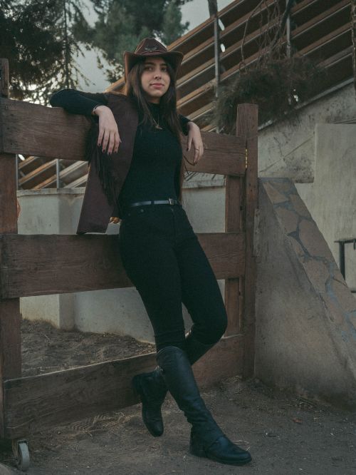 Free A woman in a cowboy hat and boots poses at a ranch. Rustic Western vibe. Stock Photo