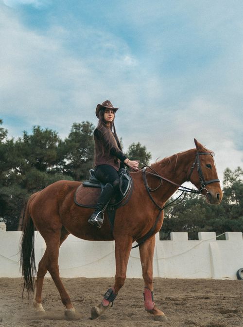 Free A woman wearing a cowboy hat rides a horse at an equestrian center under a cloudy sky. Stock Photo