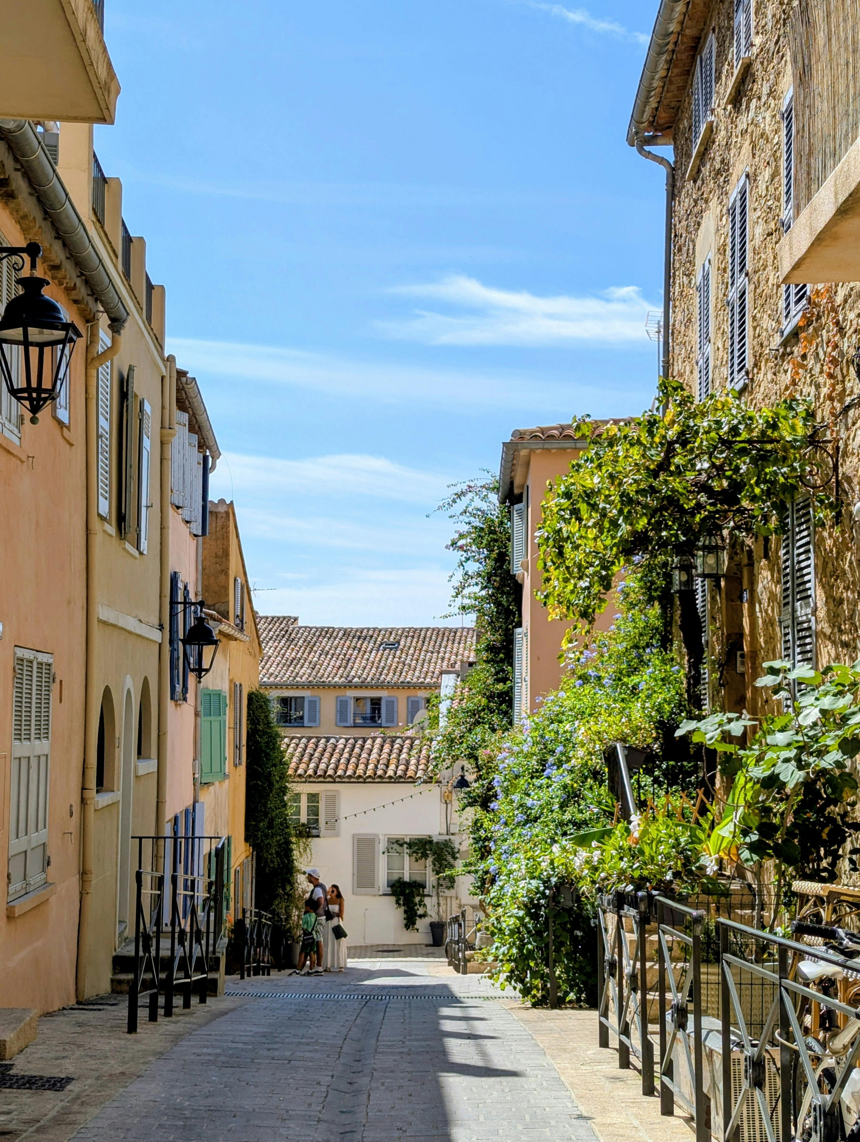 Quaint European street scene featuring warm buildings and lush greenery under a clear sky.