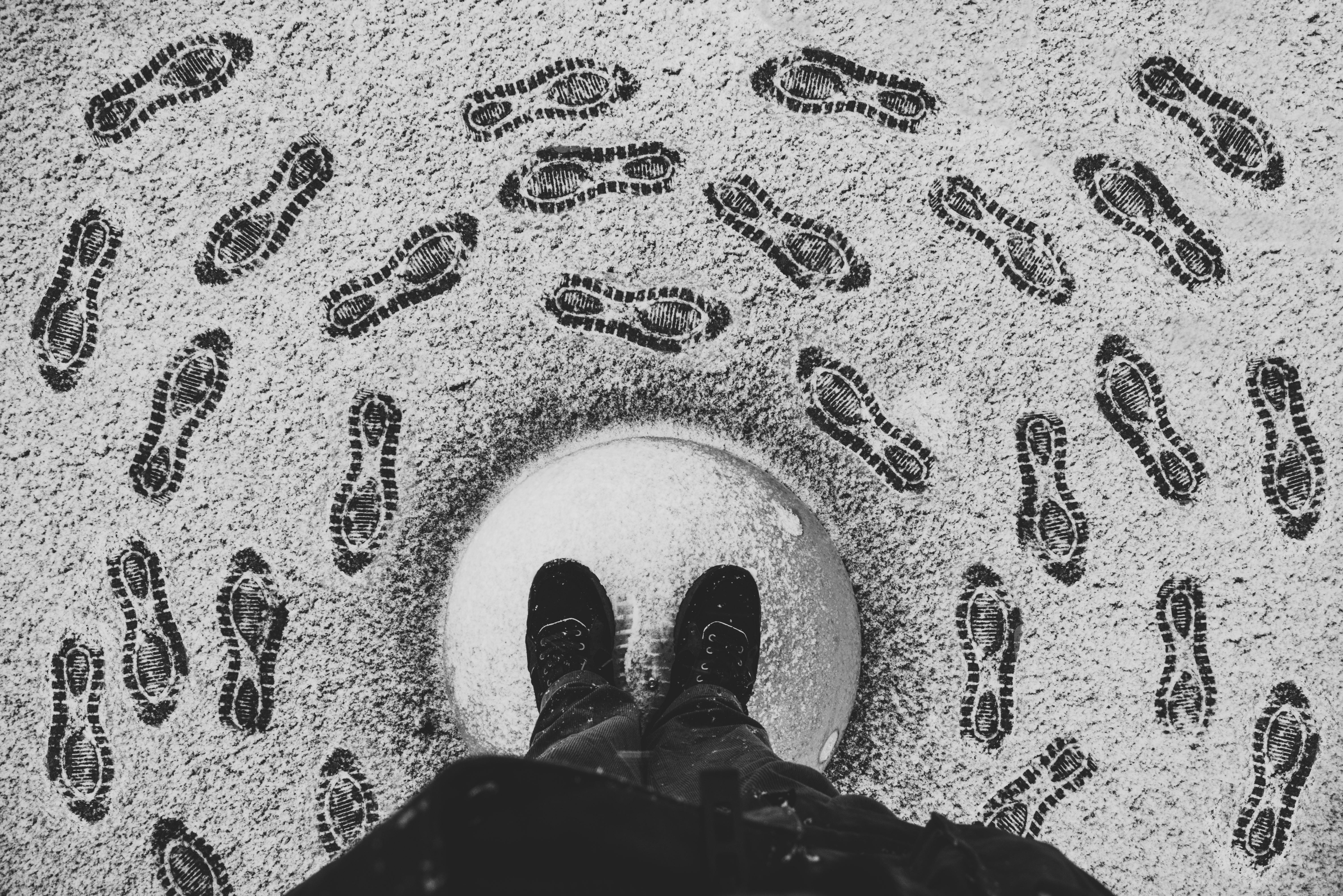 Artistic black and white photo of footprints forming a circle in the snow, with a central perspective view.