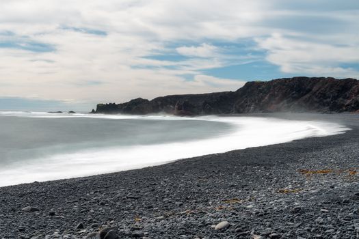 Serene view of a rocky beach with soft ocean waves and blue skies.