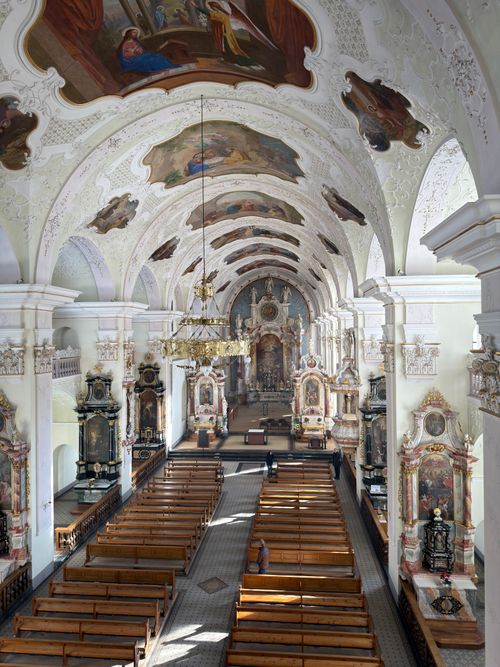 Free Stunning interior view of a Baroque church with decorative ceiling and empty pews, sunlight streaming in. Stock Photo