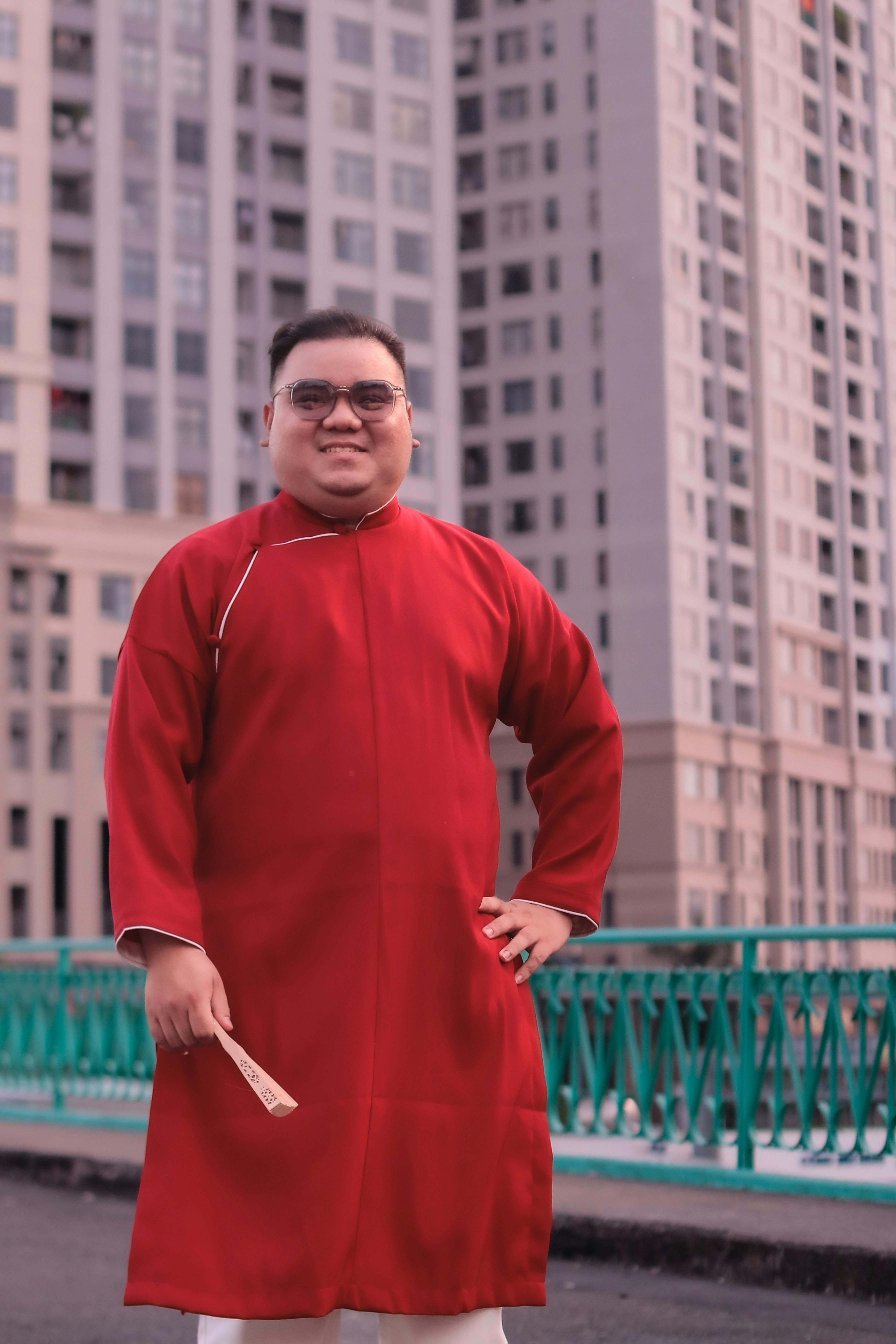 Gratis Un uomo vestito con il tradizionale abito rosso si erge con sicurezza davanti ai grattacieli. Foto a disposizione