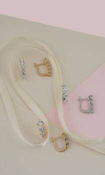 Elegant gold and silver earrings with diamonds on a pastel paper backdrop with ribbon.