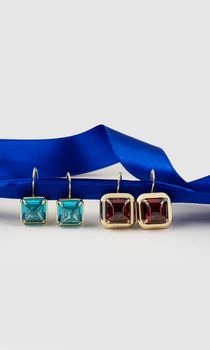 Stylish gold-framed gemstone earrings next to a vibrant blue ribbon.