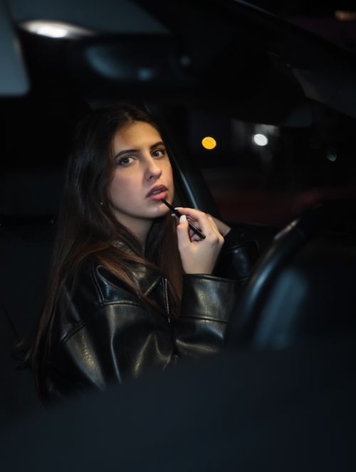 Free Young woman applies lipstick in a dimly lit car, highlighting nighttime aesthetics. Stock Photo