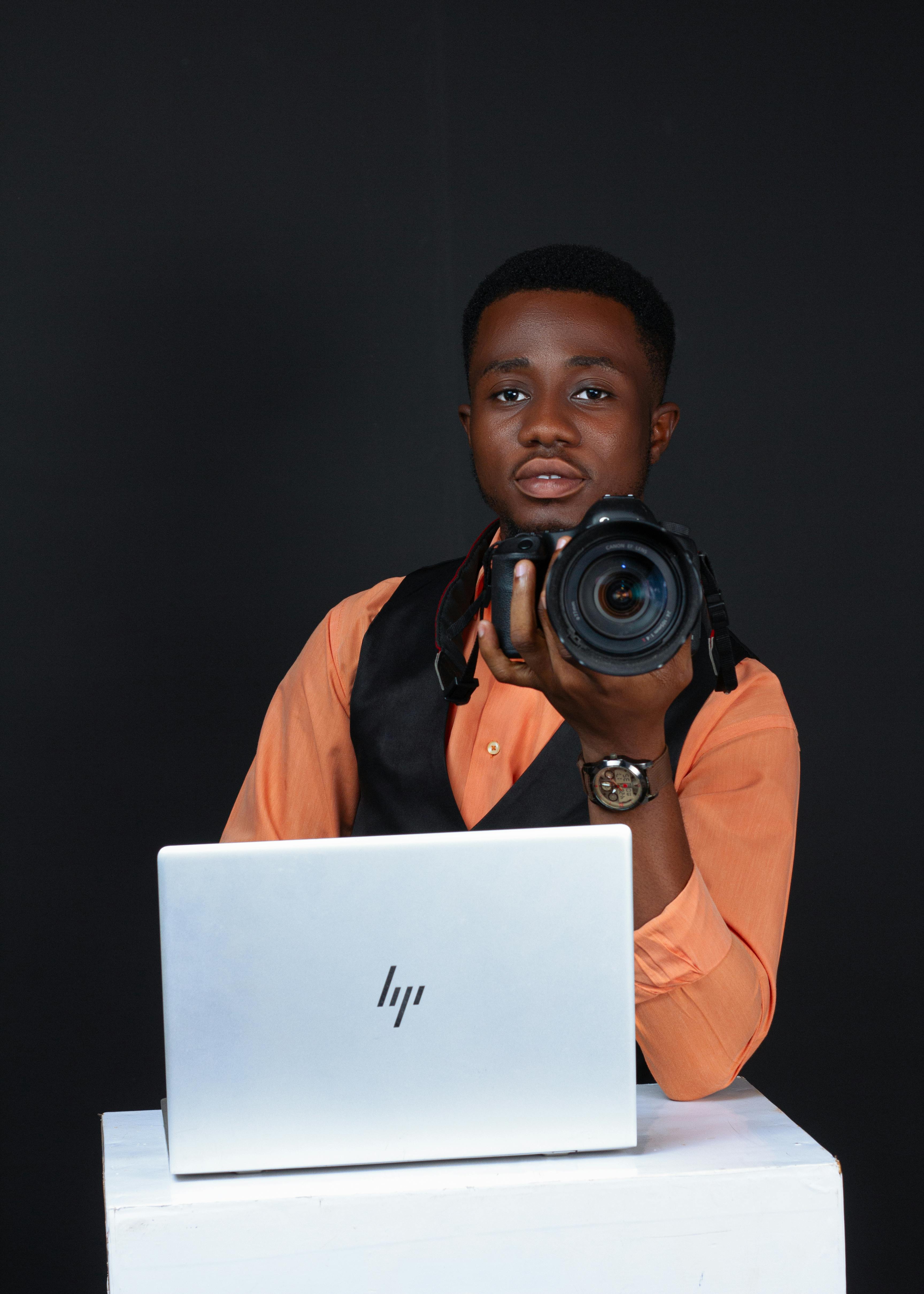Portrait of young male photographer holding a camera with a laptop on a table.