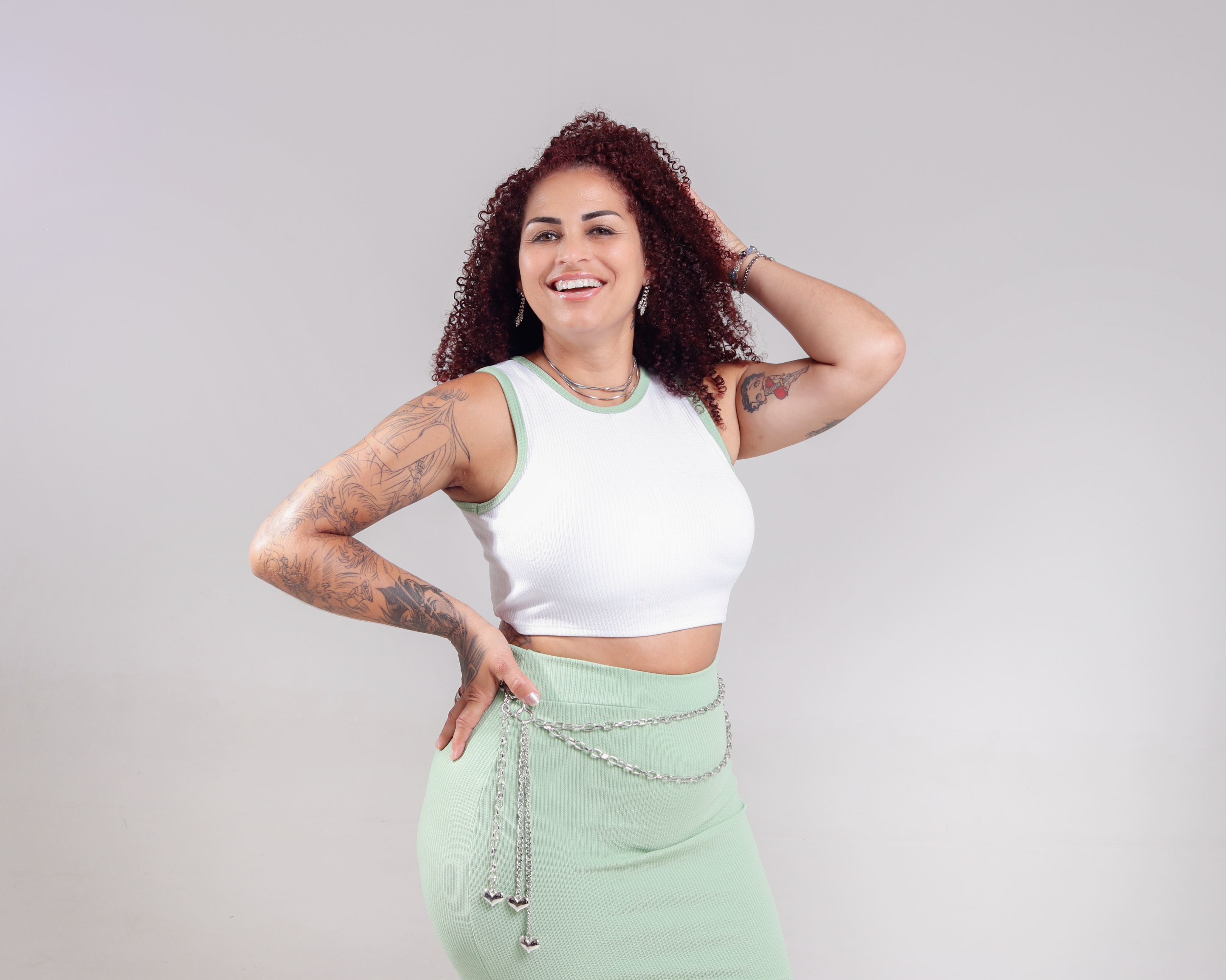 Smiling woman with tattoos and curly hair posing confidently indoors.