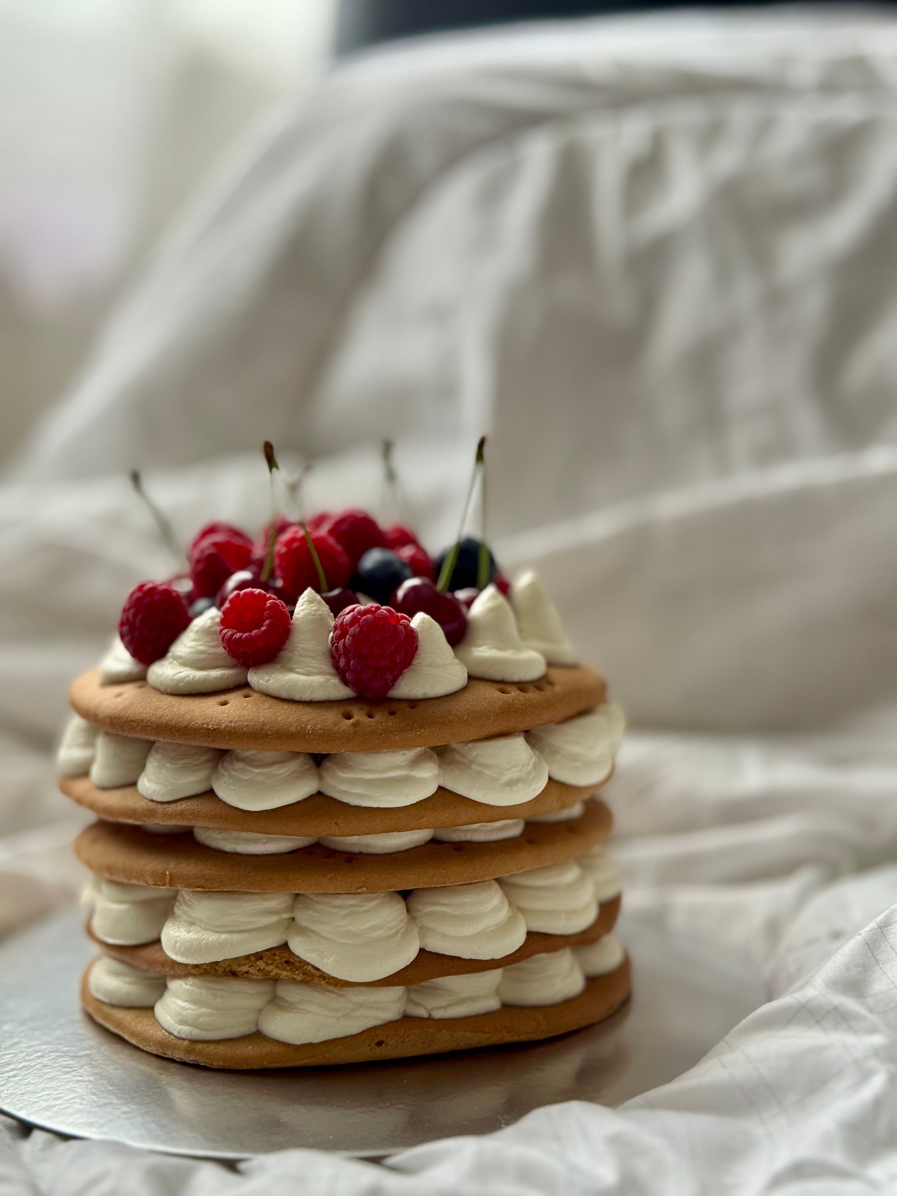 A tasty layered cake adorned with fresh raspberries and cherries, set against a soft white backdrop.