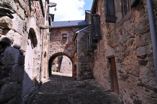 Quaint stone alleyway in a rustic village, showcasing historical architecture under blue skies.