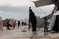 A woman sweeps in a Gaza refugee camp with children playing nearby.