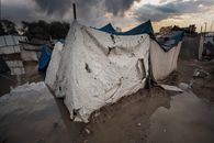 A damaged tent shelter in a flooded area of a Gaza refugee camp under stormy skies.