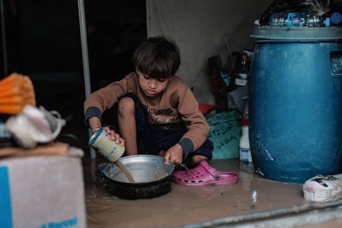 Free A young child in Gaza sits in a tent mixing food in difficult conditions, highlighting poverty. Stock Photo