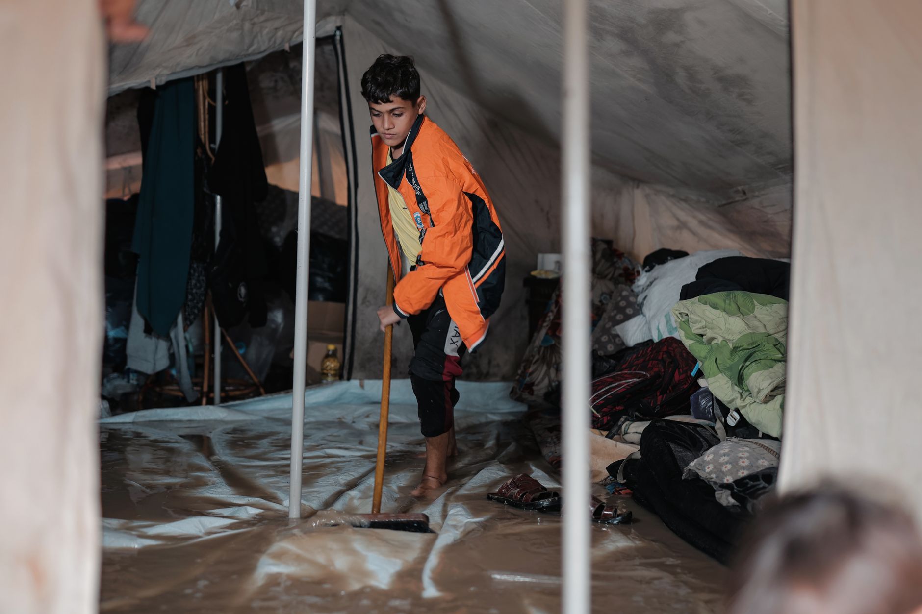 A young boy sweeps the floor inside a tent in a refugee camp in Gaza, highlighting resilience and daily life.