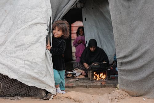 Free A young girl joyfully peering out of a tent in Gaza, with family members inside. Stock Photo