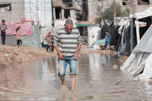 Free Middle-aged man in Gaza navigates flooded street with resilience, reflecting life challenges. Stock Photo