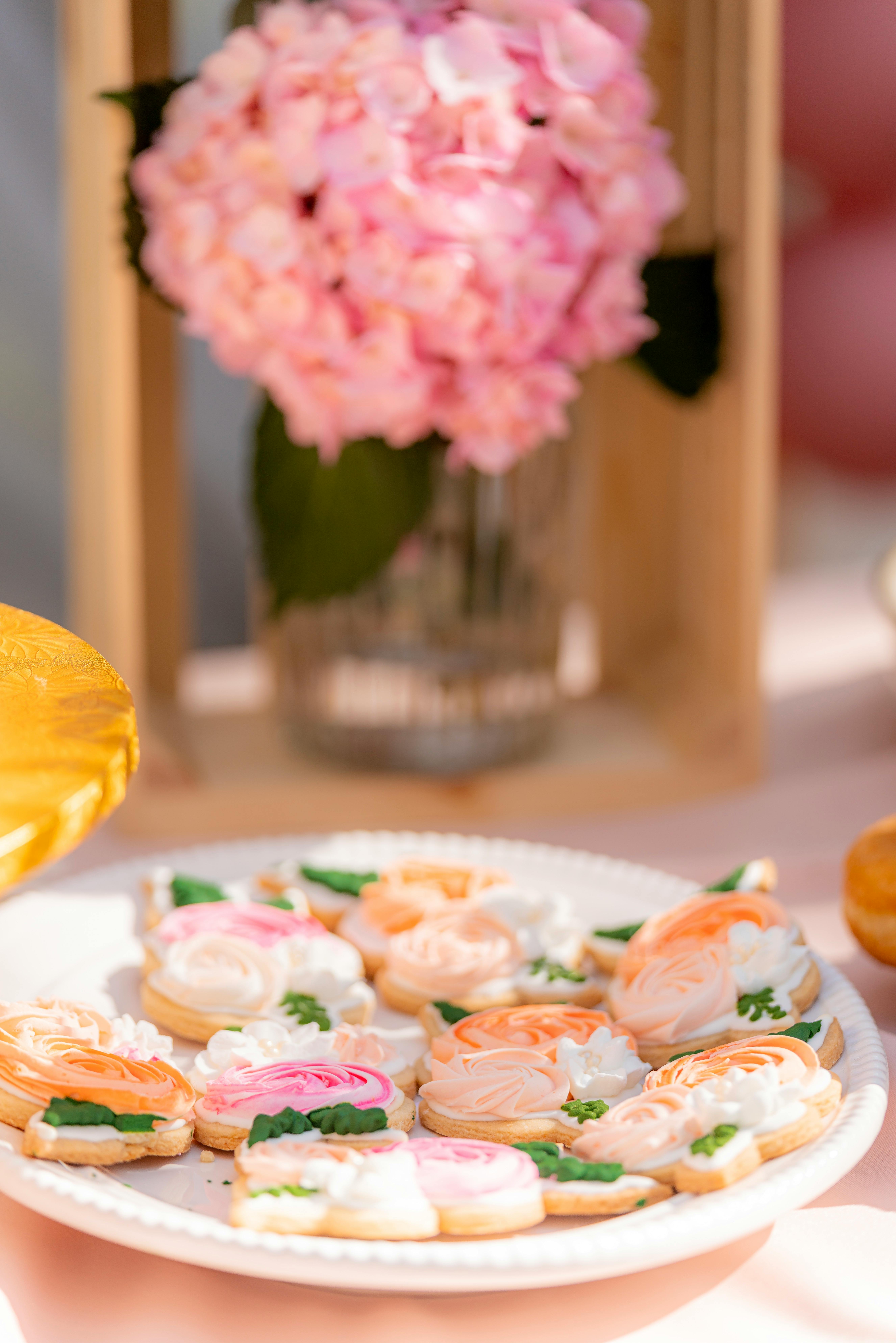 Beautifully decorated floral cookies on a plate with pink hydrangea background.