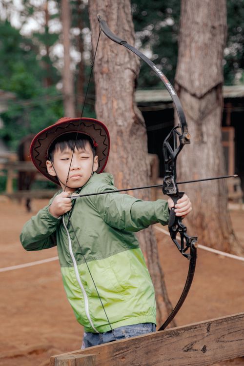 Free A young boy in a cowboy hat focuses on archery in an outdoor setting in Kon Tum, Vietnam. Stock Photo