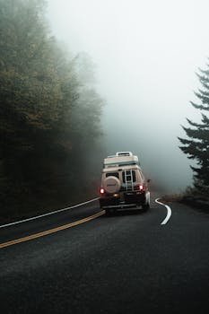 一辆露营车驶过雾气缭绕的乡村道路，营造出宁静的冒险氛围