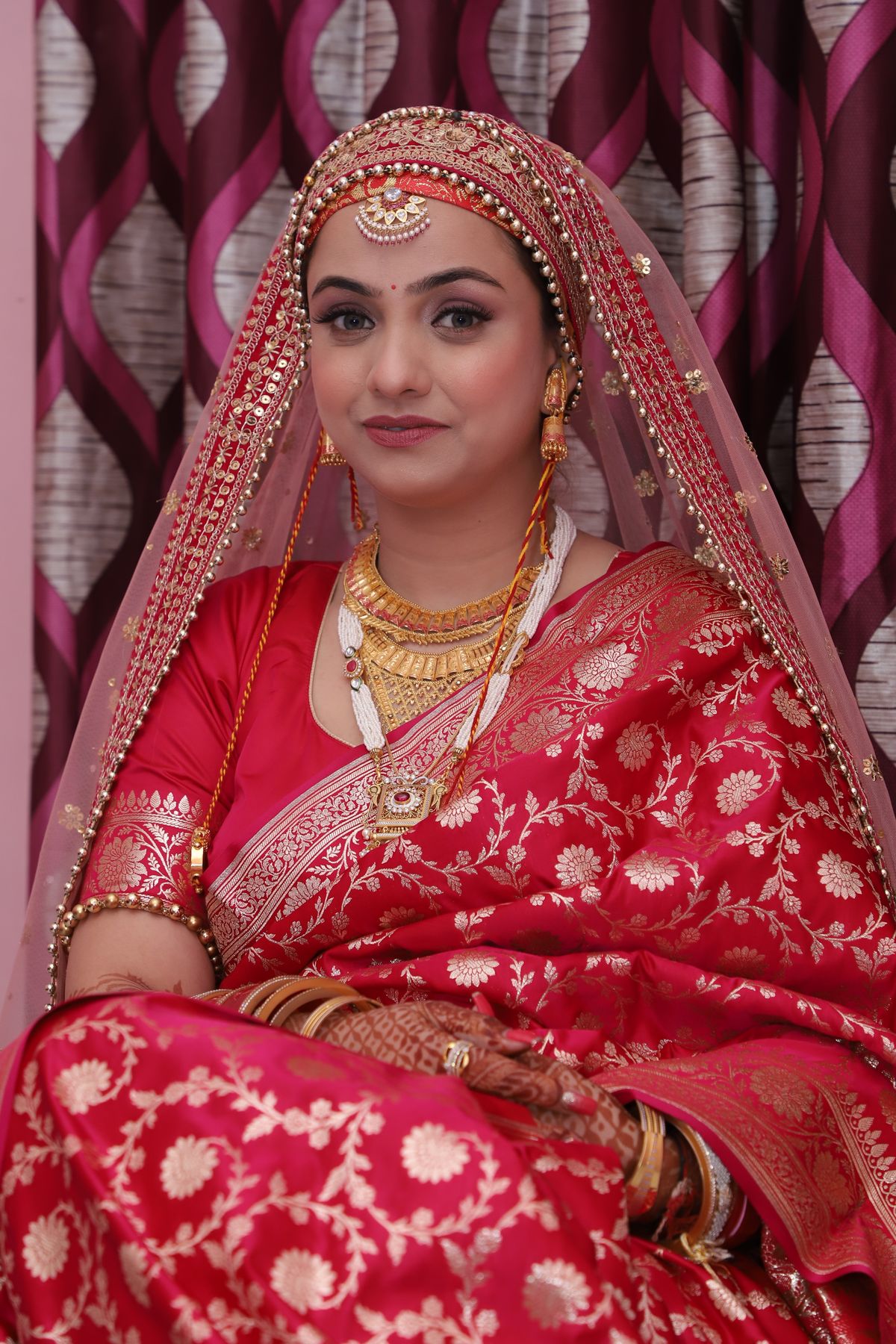 Bride in a red Banarasi saree and veil with gold jewellery