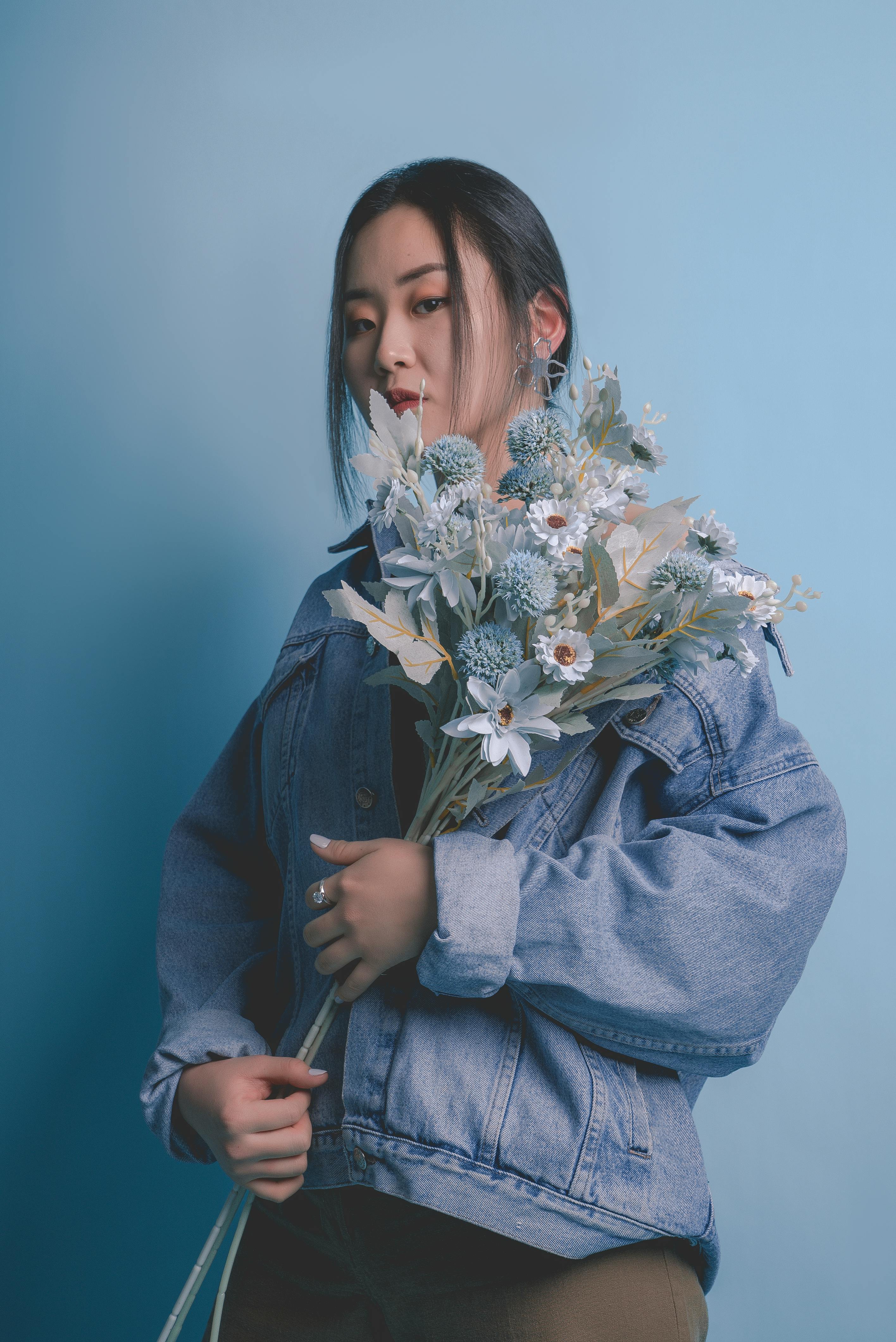 这幅肖像画描绘了一位手持精致花束的女子，背景是柔和的蓝色，画面宁静