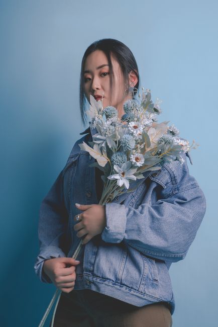 A serene portrait of a woman holding a delicate floral bouquet, set against a soft blue background.