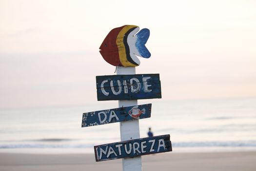 Colorful beach sign in Guaratuba, Brazil, promoting nature care at sunrise by the ocean.