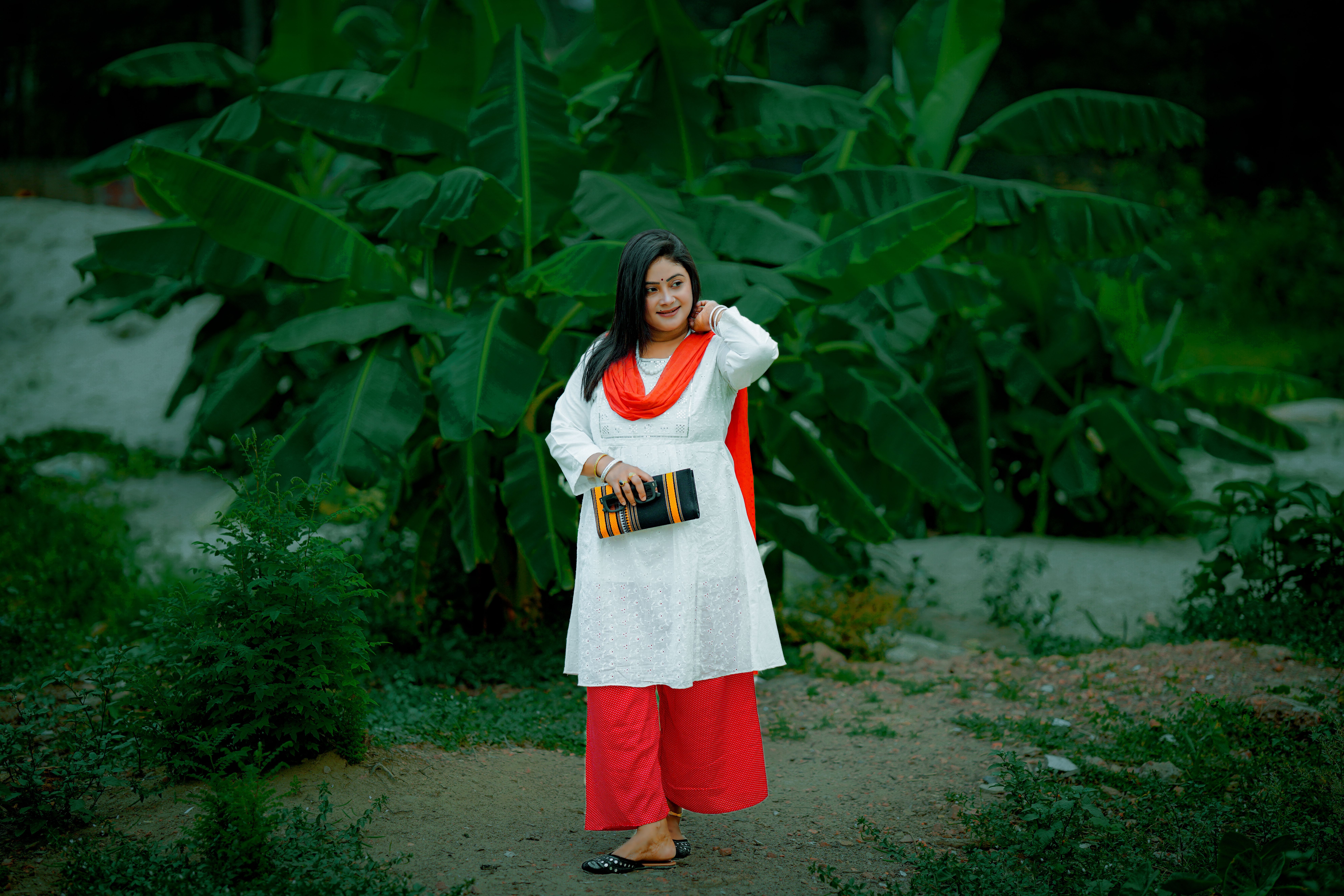 Woman poses outdoors with lush banana plants in traditional attire.