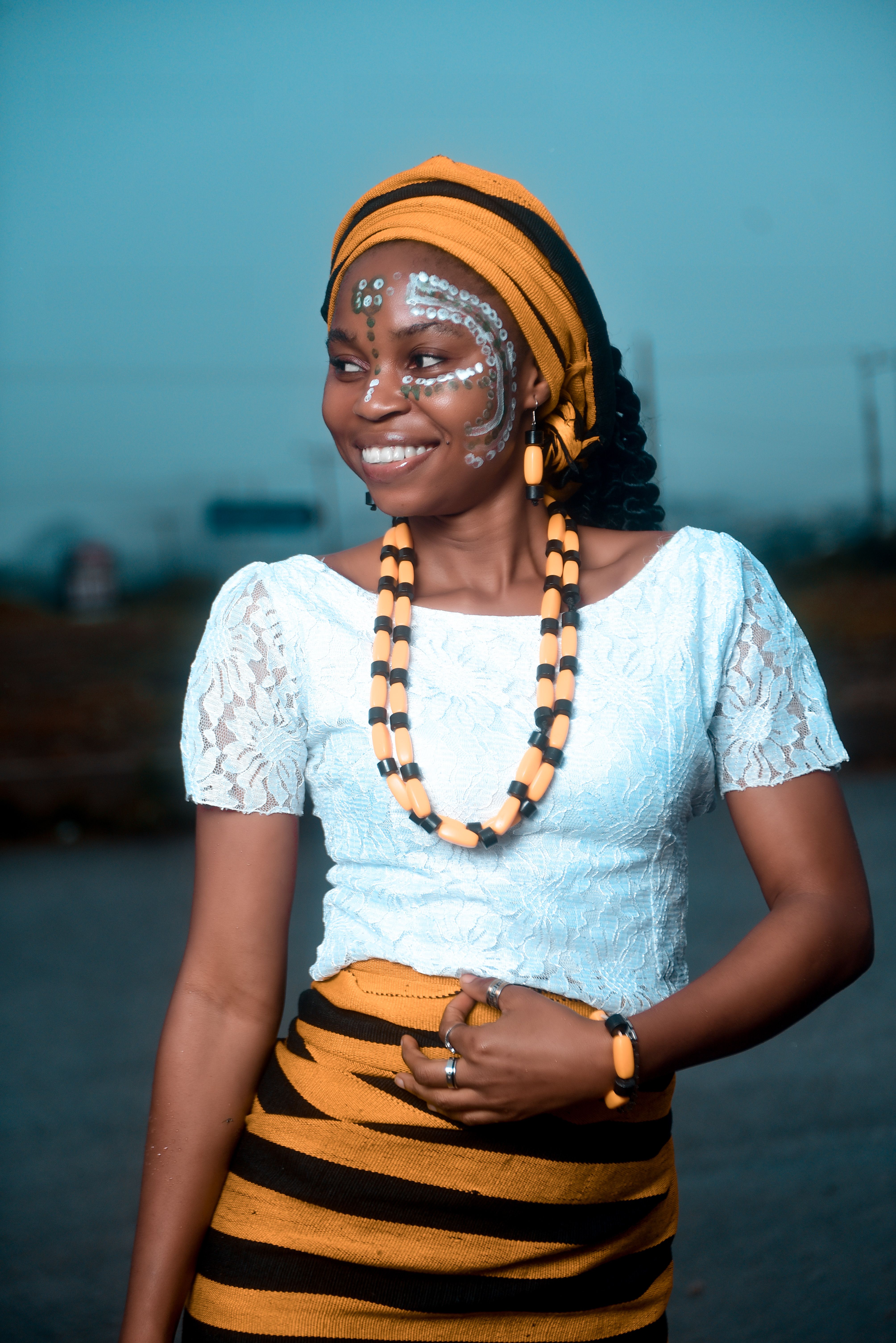Portrait of a smiling woman in traditional African attire with face paint and jewelry.