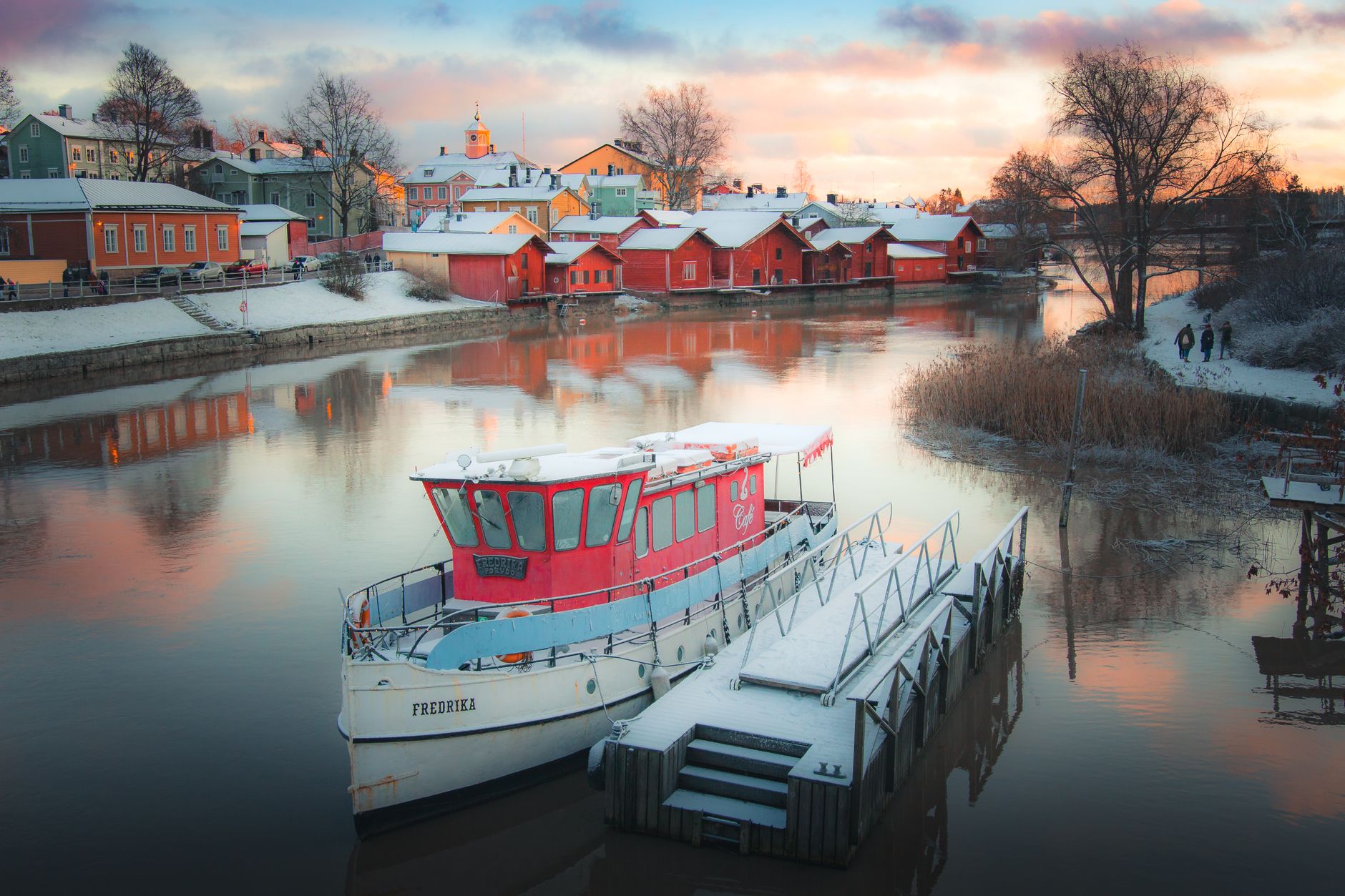 Snow-covered boats reflecting in Porvoo's historic harbor during a winter sunset.